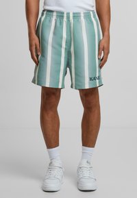 Lys grønn stripete shorts med hvite vertikale striper, elastisk liv, og ordet "KANI" brodert i mørkeblått nederst til venstre.