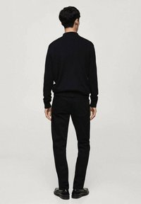 Zwarte gebreide trui met een ronde hals en geribbelde manchetten, gecombineerd met zwarte slim-fit jeans en zwarte schoenen, gezien vanaf de achterkant.