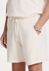 Shorts beige clair en tissu doux et texturé. Dotés d'une taille élastique avec cordon de serrage et de poches latérales.