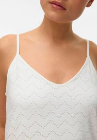 Witte mouwloze top met een V-halslijn, een textuur in golfpatroon met uitsparingen, en dunne schouderbandjes.