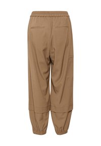 Pantalon marron coupe ample avec taille et poignets élastiques, deux poches passepoilées à l’arrière et une poche plaquée latérale sur la jambe droite.