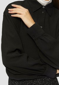 Zwarte textuur button-up shirt met een kraag en gathered mouwen, met zwarte knopen aan de voorkant en op de manchetten.