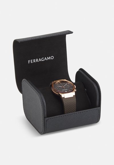 Must must musta kasti "FERRAGAMO" logo'ga, millel on kuldsete aktsentidega kell, tekstureeritud pruuni rihmaga ja tume kell Face, mis kuvab mitmeid ajanäitajaid.