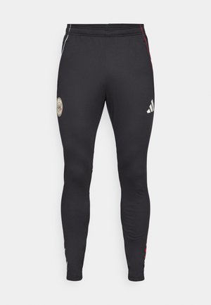 Crne sportske leggingse s prilagođenim dizajnom, s zlatnim grbom, bijelim Adidas logom i crvenim akcentnim trakama duž bočnih strana.