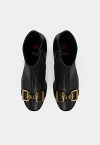 Bottes noires en cuir à la cheville avec de grands accents en boucle dorée, une texture lisse et un design épuré avec une fermeture éclair.