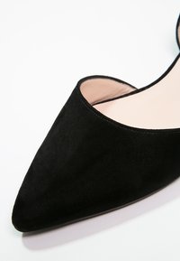Chaussure pour femme en daim noir à bout pointu avec doublure intérieure beige clair, photographiée sur un fond blanc.