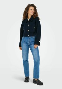 Marineblå cropped jakke med guldknapper, to forlommer og krave, parret med lyseblå lige ben jeans og sorte loafers.