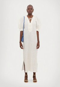 Pitkä, väljä vaate vaalea kangas, jossa on liehupaidat, nyörityskaulus ja kukkakuvio; sivuhalkio; yhdistetty siniseen laukkuun ja sandaaleihin.