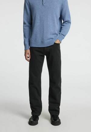 Pull en maille bleu clair avec col et un seul bouton, associé à un jean noir droit et des chaussures noires.