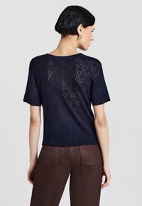 Top corto a maniche corte di colore blu navy lavorato a maglia, caratterizzato da un motivo geometrico, scollo rotondo e orlo a costine, abbinato a pantaloni fitted marroni.