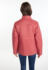 Jachetă pufoasă de culoare corai, cu un design pe verticală quiltat, guler înalt și mâneci lungi, asortată cu blugi de culoare albastru închis.