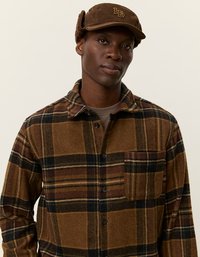 Chemise à carreaux marron avec une poche avant, fabriquée dans un tissu texturé. Casquette en velours côtelé marron assortie avec rabats d'oreilles et détail de logo.