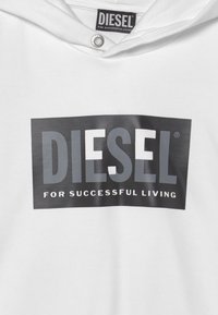 Bílá mikina s kapucí, na které je velké černé obdélníkové logo se slovem "DIESEL" a frází "PRO ÚSPĚŠNÝ ŽIVOT" bílým písmem.