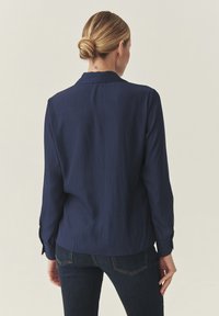 Tengerészkék, vékony csíkozású ing, hosszú ujjakkal, gombos mandzsettával és laza szabással. Klasszikus gallérral és sima textúrával rendelkezik.