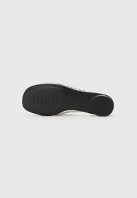 Sandal med en genomskinlig ovandel med flera remmar, en vadderad sula och en texturerad svart gummisula för bra grepp.
