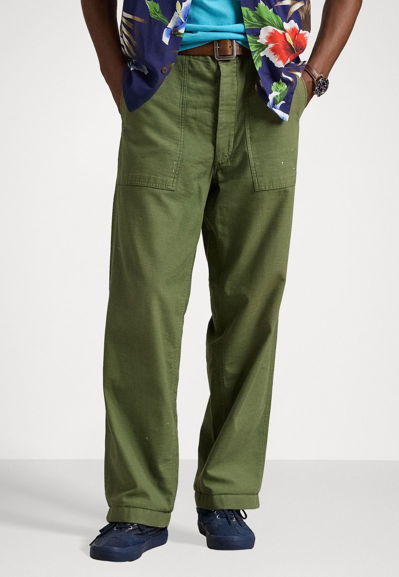 Pantalones cargo de algodón verde, con un corte holgado, que cuentan con bolsillos laterales y un diseño de pierna recta, combinados con zapatos azul oscuro.
