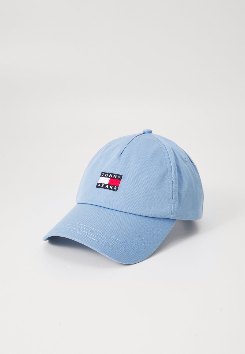 Lyseblå baseballcap med en buet skygge, der har et rektangulært Tommy Jeans-logo i rød, hvid og sort på forsiden. Tekstur af bomuldsstof.