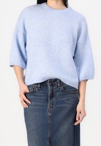 Pull tricot bleu clair à coupe ample, col côtelé et manches courtes, associé à une jupe en denim foncé. Texture douce, design décontracté.