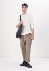 Biały sweter wykonany na drutach, beżowe spodnie z kordurowej tkaniny, czarne buty i ciemna torba na ramię. Prosty design, naturalne tekstury i neutralne kolory.