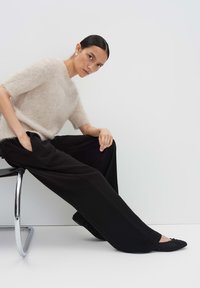 Pull en mohair beige clair mélangé, coupe décontractée avec des manches courtes, associé à un pantalon large noir et des chaussures plates noires. Design minimaliste.