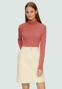 Langsleeve turtleneck top in rozenkleur, gecombineerd met een crèmekleurige rok tot de knie met een knoop en voorzakken. Over het geheel een gladde textuur.