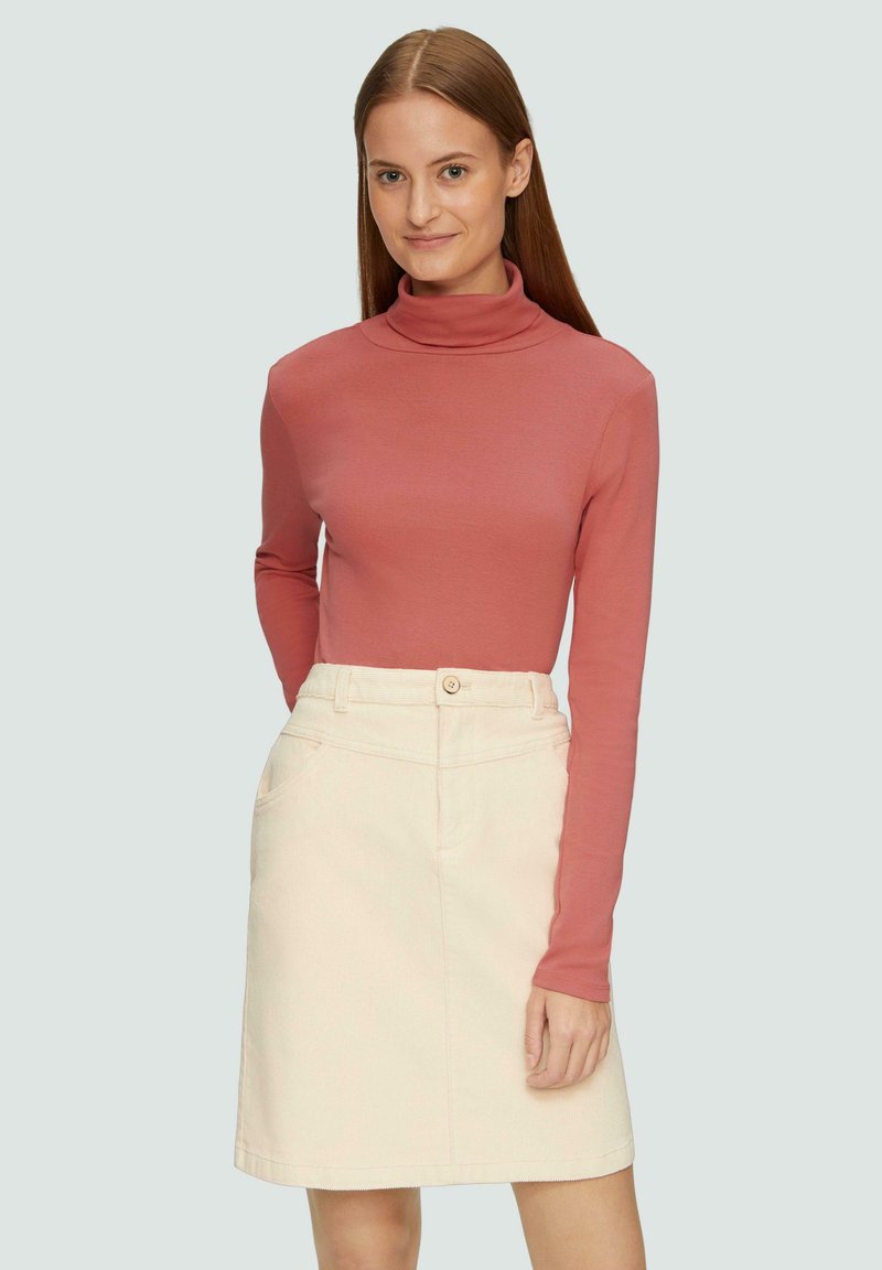 Langsleeve turtleneck top in rozenkleur, gecombineerd met een crèmekleurige rok tot de knie met een knoop en voorzakken. Over het geheel een gladde textuur.