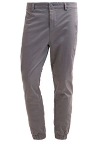 Grijze taps toelopende broek met knoopsluiting, riemlussen, steekzakken en elastische boorden bij de enkels.