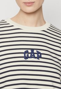 Gestreiftes Baumwoll-T-Shirt in Creme und Marineblau, mit Rundhalsausschnitt und gummiertem "GAP"-Logo in Marineblau auf der Brust.