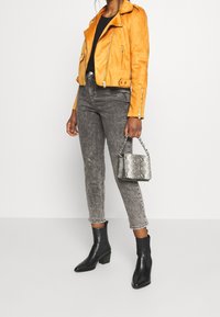 Chaqueta de biker de ante naranja, top negro, jeans grises, botas negras hasta el tobillo, bolso de mano plateado con estampado de serpiente, corte ajustado, material texturizado.