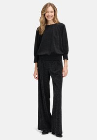 Pull noir pailleté à coupe décontractée et manches raglan, assorti à un pantalon large noir pailleté, porté avec des chaussures noires.