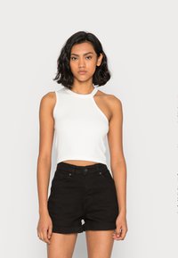 Top cropped branco sem mangas com decote arredondado e recortes nos ombros, combinado com calções de ganga pretos de cintura alta com barras enroladas.