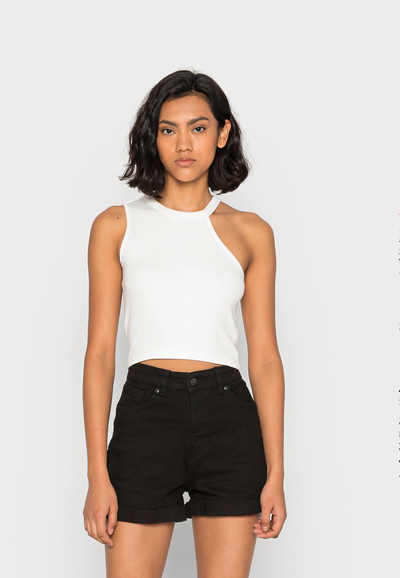 Top cropped branco sem mangas com decote arredondado e recortes nos ombros, combinado com calções de ganga pretos de cintura alta com barras enroladas.