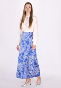 Lange, blauwe paisley rok van soepel materiaal, versierd met witte ingewikkelde patronen. Gecombineerd met een witte blouse en zilveren hakken.