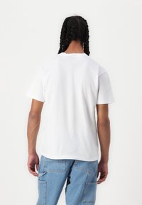 Tricou alb din bumbac, cu o croială lejeră și mâneci scurte, având un guler rotund, țesătură texturată și un design simplu.