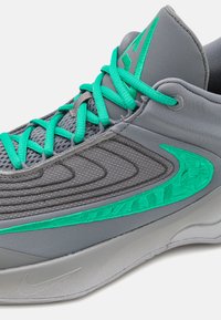 Grå atletiksko med en struktureret mesh-overdel, turkise snørebånd og en broderet teal-accent på siden, samt en glat grå sål.