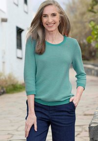 Türkisen gestreifter Pullover mit Dreiviertelärmeln, geripptem Halsausschnitt und Saum, kombiniert mit dunkelblauen Hosen. Der Stoff wirkt weich und strukturiert.