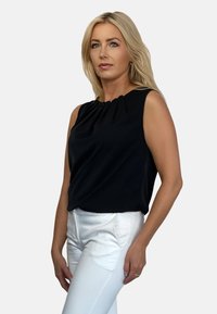 Czarna bezrękawnikowa bluzka z plisowanym dekoltem, wykonana z gładkiego materiału. Połączona z białymi, dopasowanymi spodniami ze strony, posiadającymi kieszenie.