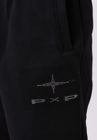 Primo piano di un tessuto nero con una tasca e un design a forma di stella luccicante sopra un logo "PXG" con borchie.