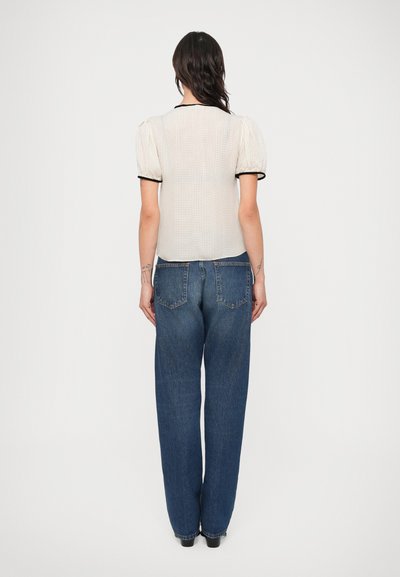 Ljusfärgad, texturerad blus med puffärmar och svart kant, kombinerad med högmidjade, löst sittande blå jeans.