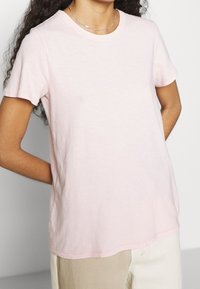 Light pink short-sleeve t-shirt made from soft fabric, featuring a round neckline and a relaxed fit. Smooth texture with side slits.