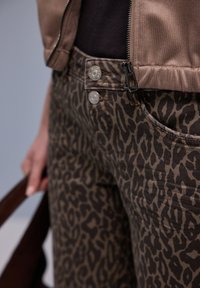 Ruskeat leopardikuvioiset housut, joissa on kapea malli, kaksi nappisuljetta ja etutasku. Kangas on sileäpintainen.