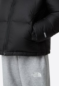 Svart dunjakke med glidelås foran, med strukturert finish og isolert padding. Kombinert med lysegrå joggebukser med logo.