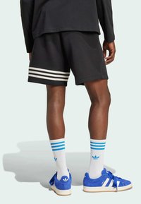 Shorts sportivi neri con strisce triple bianche, calze bianche con strisce blu e sneakers blu con accenti e logo bianchi.