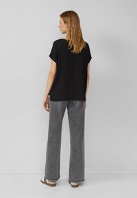 Zwart top met korte mouwen van textuurstof, gecombineerd met hoge, grijze wijde jeans en beige sneakers met donkere accenten.
