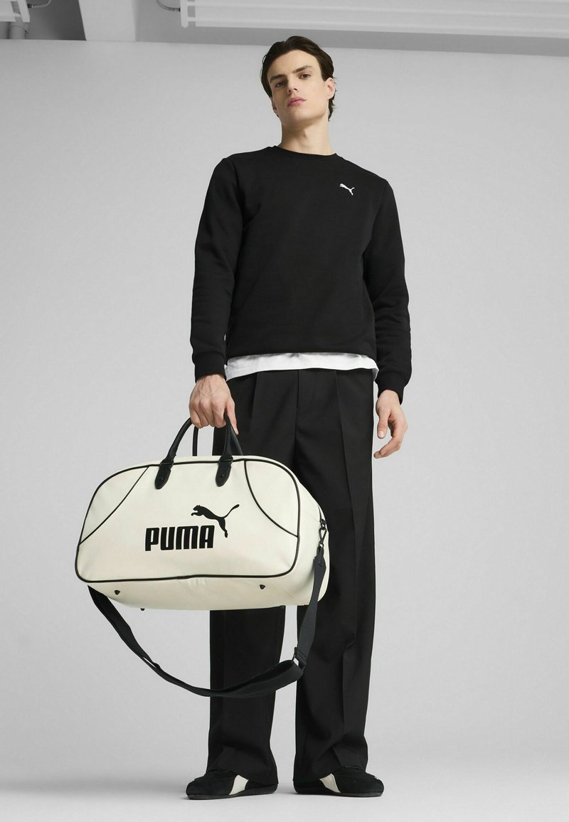 Sac de sport blanc avec des accents noirs, arborant un logo "PUMA" bien visible, de forme arrondie, avec deux poignées supérieures et une bandoulière réglable.