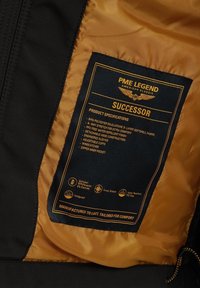 Doublure noire et orange de veste avec étiquette PME Legend Successor listant le tissu, les caractéristiques et les détails d'entretien à l'intérieur du vêtement.