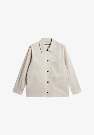 Lys beige jakke med kravehals, sorte knapper og tre forlommer. Fremstillet af glat stof, med lange ærmer.