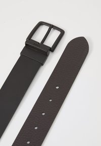 Ceinture en cuir noir avec une finition texturée, dotée d'une boucle rectangulaire en métal noir gravée "BOSS". Comprend des trous pour le réglage.
