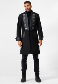 Schwarzer Wildledermantel mit Lederkragen und Knopfdetails. Verfügt über eine figurschmeichelnde Passform, Seitentaschen und lange Ärmel.