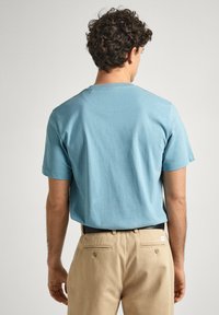 Jasnoniebieska bawełniana koszulka z krótkimi rękawami i okrągłym dekoltem. Noszona z beżowymi spodniami, prezentująca prosty design i gładką fakturę.